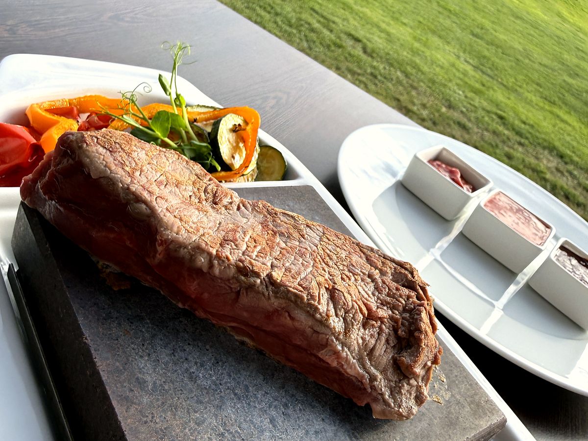 Steak vom eigenen Hof auf dem heißen Stein, daneben Grillgemüse, Dips und der Blick über den Platz
